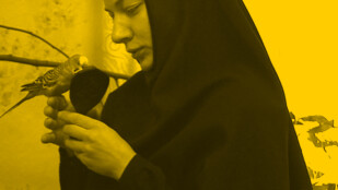 Zdjęcie: kobieta w czarnym stroju zakonniczki prawosławnego kościoła, w dłoni trzyma papużkę i lusterko, w tle gałązka