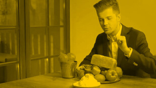 Czarno-żółte zdjęcie. Radek Kotarski siedzi przy stole. Na stole leży miska owoców i chleb.