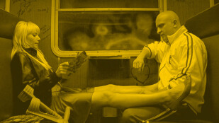 Czarno-żółty kadr z filmu „Wojna polsko-ruska”. Wagon w pociągu. Łysy Borys Szyc siedzi na przeciwko Romy Gąsiorowskiej. Roma czyta gazetę i trzyma nogi na jego kolanach. Borys patrzy na jej nogi. Jest ubrany w ortalionową kurtkę. Na wprost pociągowe okno.
