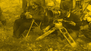 Zdjęcie: W centralnym punkcie kamera na niskim obiektywie. Obok niej trzy osoby, po lewej Jerzy Hoffman, siedzi na biwakowym krześle, dalej kuca Józef Letkier, do wizjera kamery przykłada oko Jerzy Gościk.