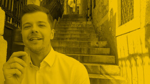 Czarno-żółte zdjęcie. Radek Kotarski w koszuli patrzy w obiektyw, uśmiecha się i gestykuluje. W tle schody.